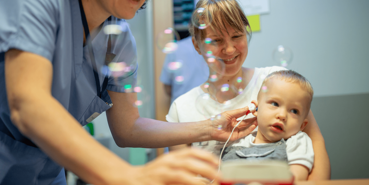 Enfant qui passe un test auditif dans les bras de sa mère